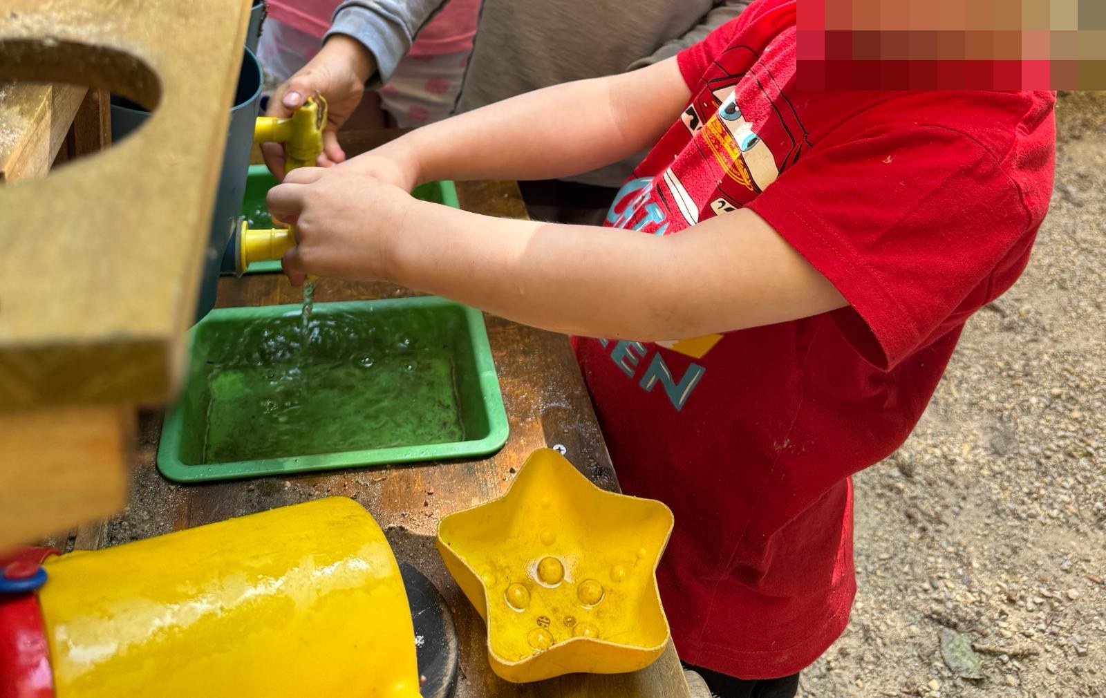 Kind spielt an der Matschk&uuml;che mit Wasser