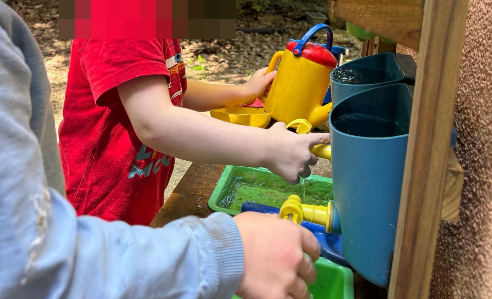 Zwei Kinder pumpen und gie&szlig;en Wasser an der Matschk&uuml;che