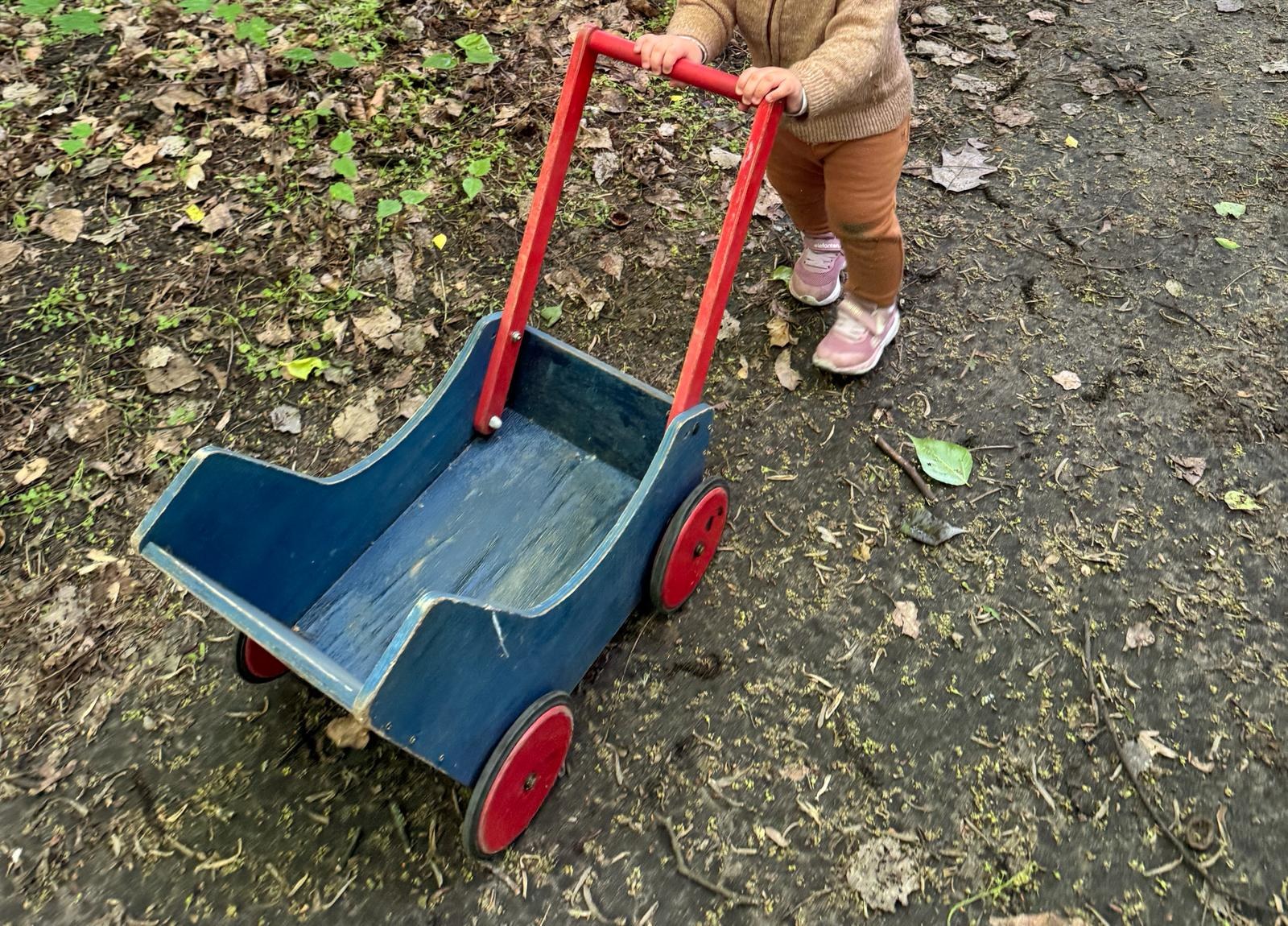 Kleinkind schiebt einen h&ouml;lzernen Laufwagen durch den Garten