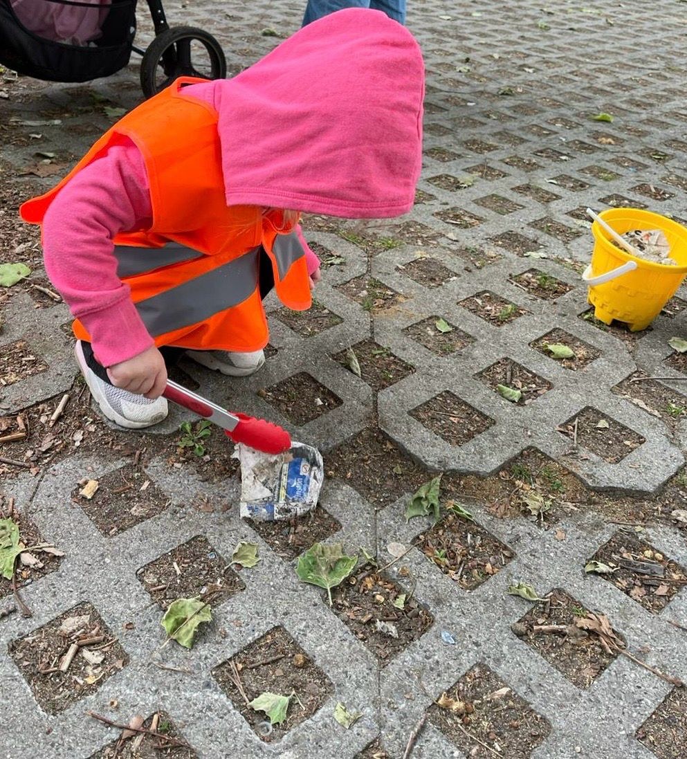 Kind in Warnweste sammelt mit einer Greifzange M&uuml;ll auf