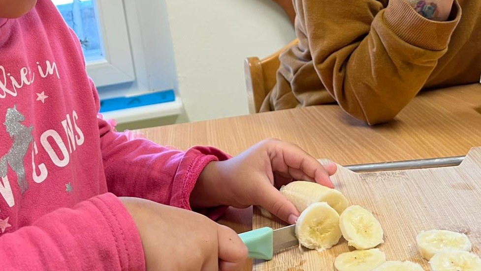 Kind schneidet selbstst&auml;ndig eine Banane in Scheiben